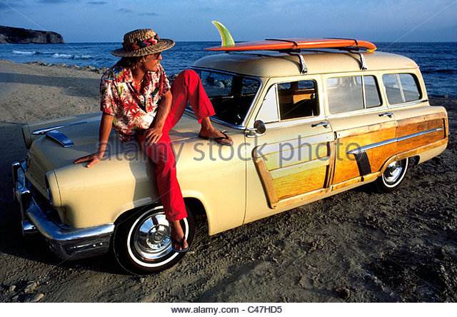 a-california-surfer-relaxes-on-his-woodie-station-wagon-as-the-sun-c47hd5