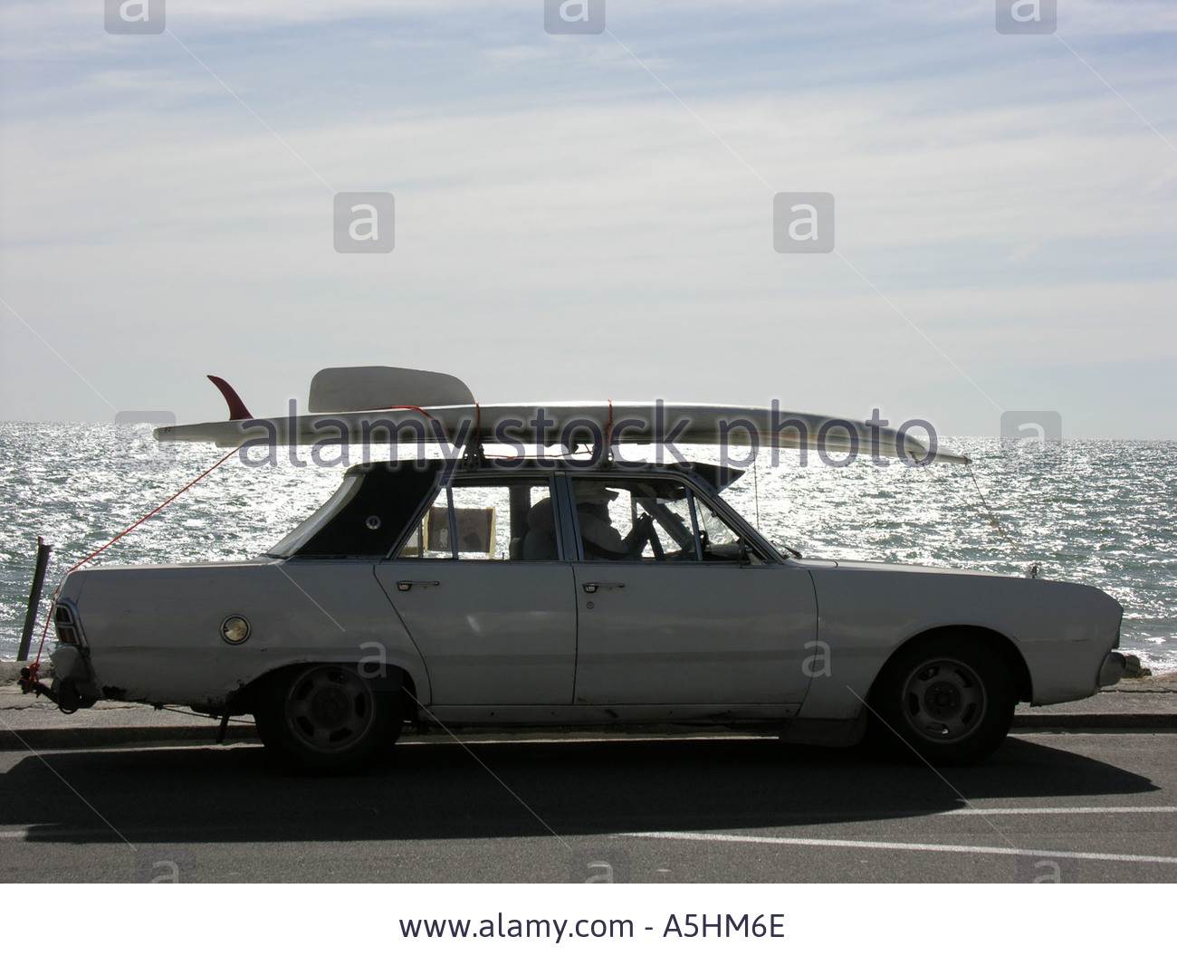 old-convertible-car-with-surfboard-on-roof-driving-on-esplanade-A5HM6E