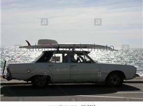 old-convertible-car-with-surfboard-on-roof-driving-on-esplanade-A5HM6E