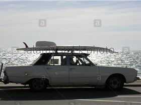 old-convertible-car-with-surfboard-on-roof-driving-on-esplanade-A5HM6E
